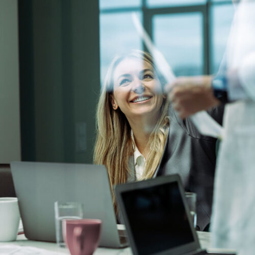 E-Learning kursus i projektledelse. Kvinde smiler op på person, der fremlægger.