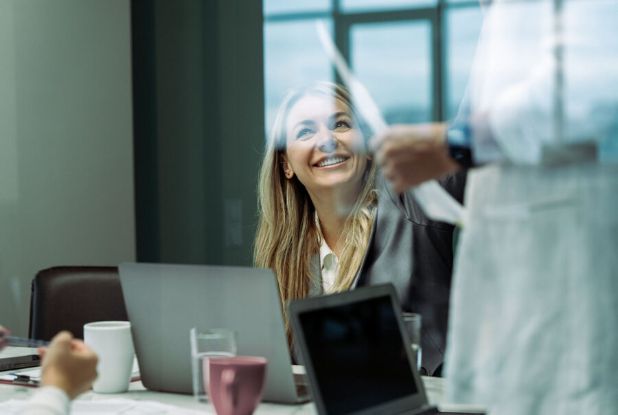 E-Learning kursus i projektledelse. Kvinde smiler op på person, der fremlægger.