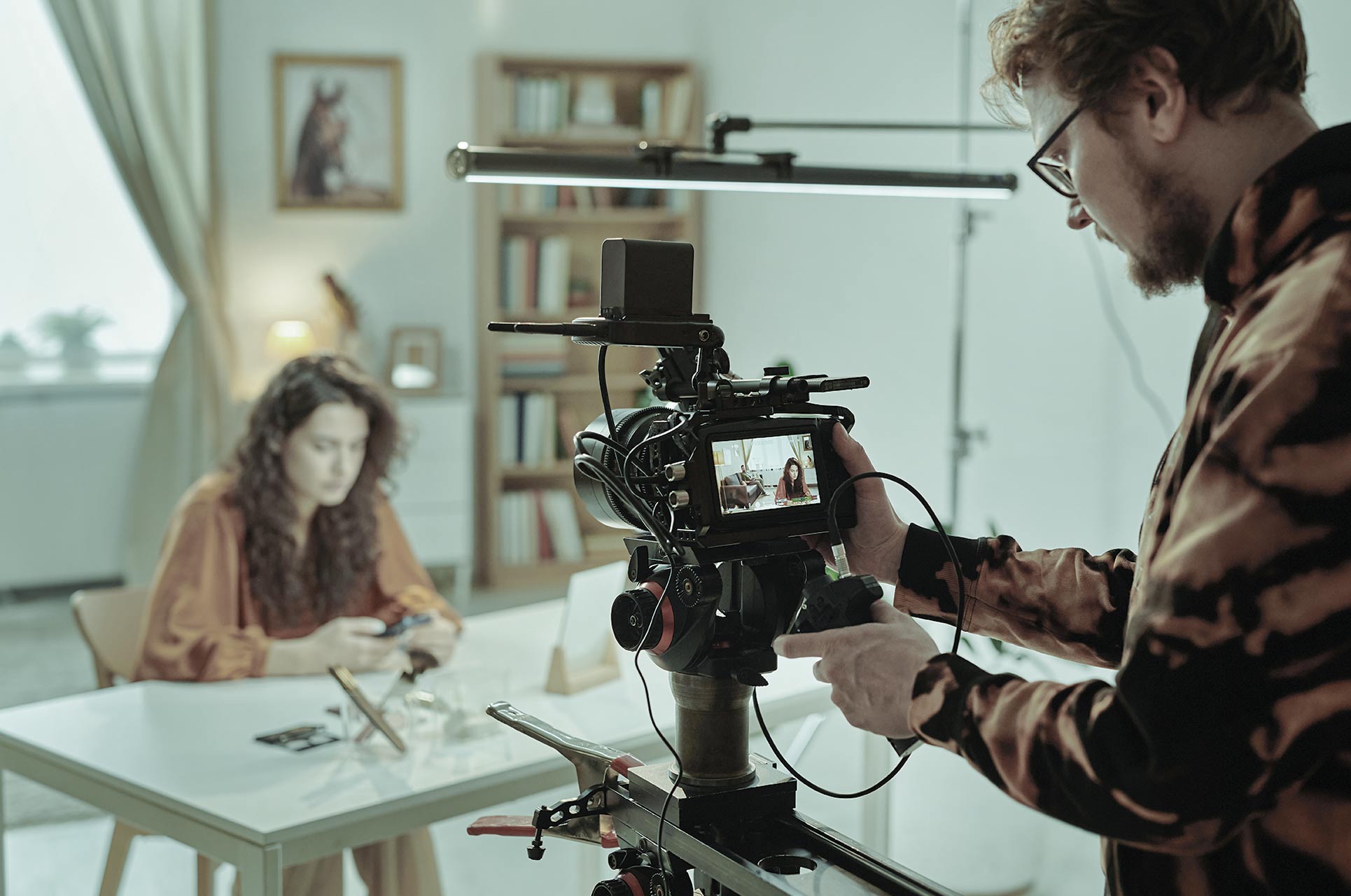 Behind the scenes af en videoproduktion til et E-Learning. Mand bag kamera optager kvinde ved bord.